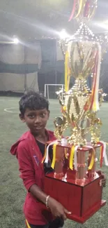 Boy holding a large trophy on a soccer field.