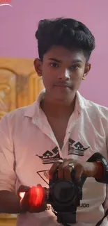 Young man holding a camera with a vibrant pink background.