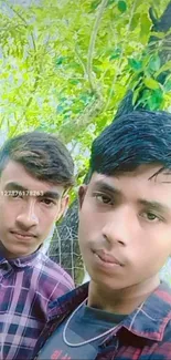 Two young men posing outdoors with green foliage background.