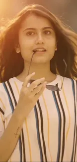 Young woman in striped shirt under sunset light, peaceful expression.