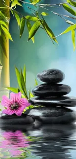 Stacked stones with bamboo and pink flower reflected in water.