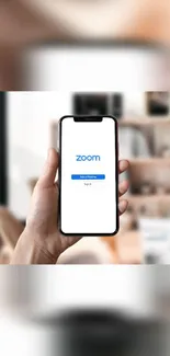 Hand holding smartphone displaying Zoom app in a modern room.